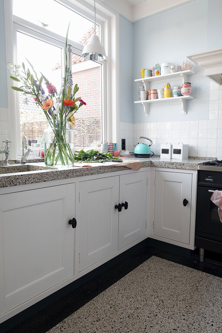 Bright kitchen with white cupboards and colourful bouquet of spring flowers in glass vase