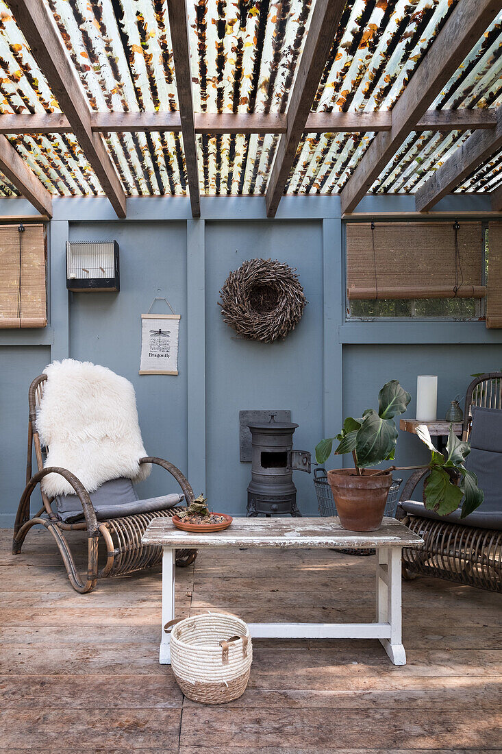 Überdachte Terrasse mit Rattansesseln, Holzofen und rustikalem Tisch