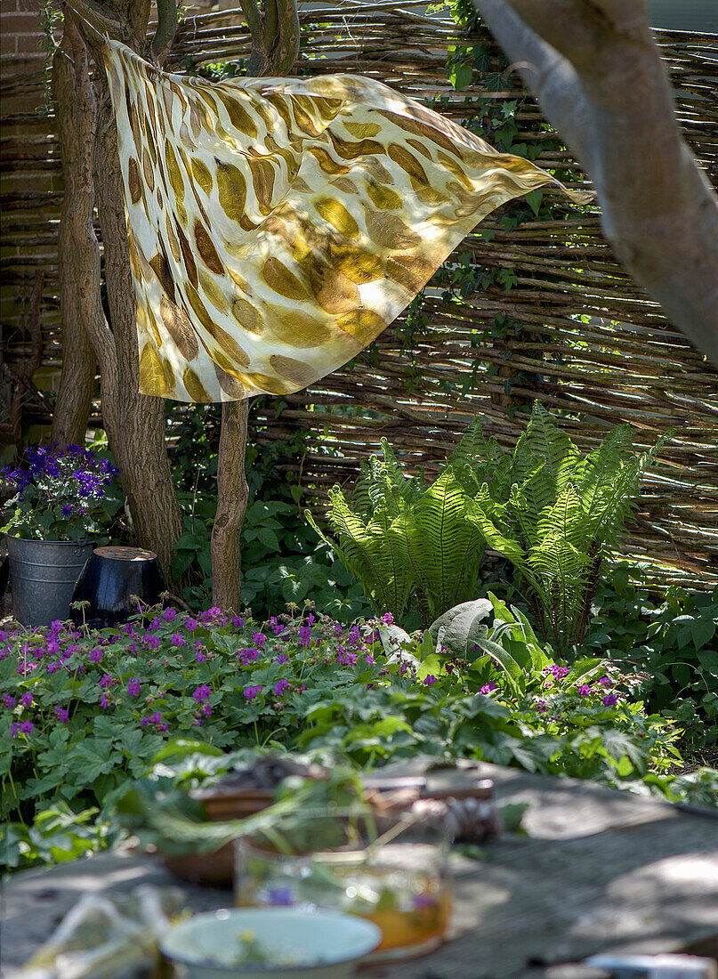 Tuch mit Pflanzendruck an Wäscheleine im Garten, Farne und Weidenzaun