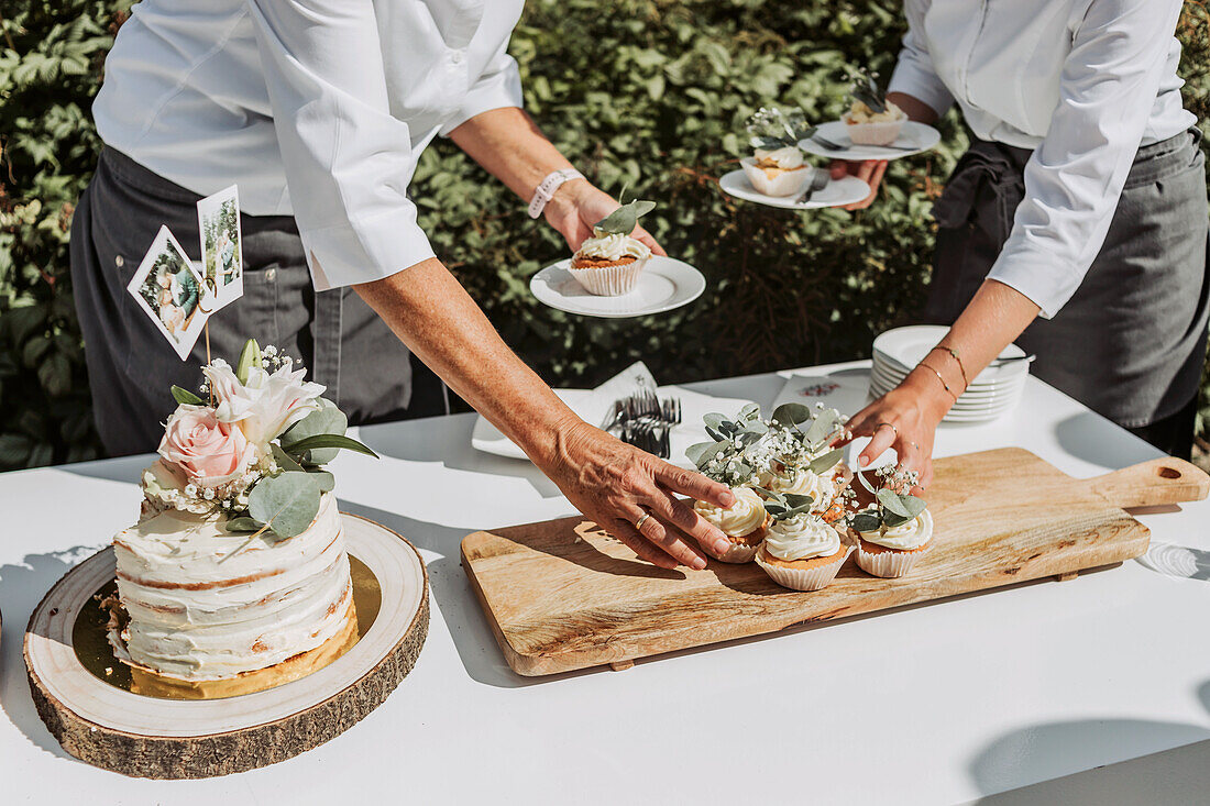 Catering staff arranging wedding cake and cupcakes on buffet