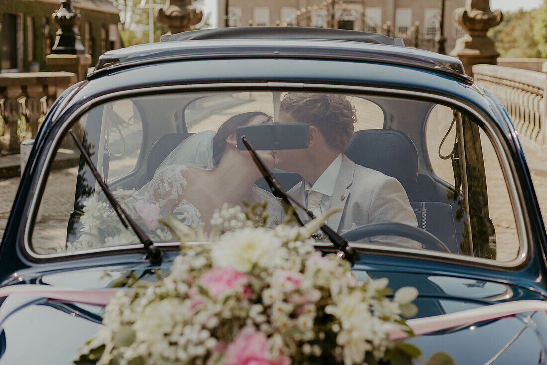 Bride and groom kissing in a vintage car decorated with floral arrangements