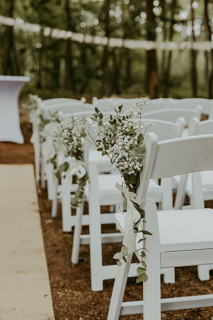 White chairs with flower arrangements for an outdoor ceremony