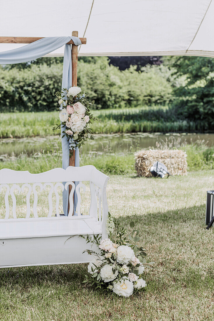 Weiße Vintage-Bank mit Blumendekoration unter einem Zelt im Garten