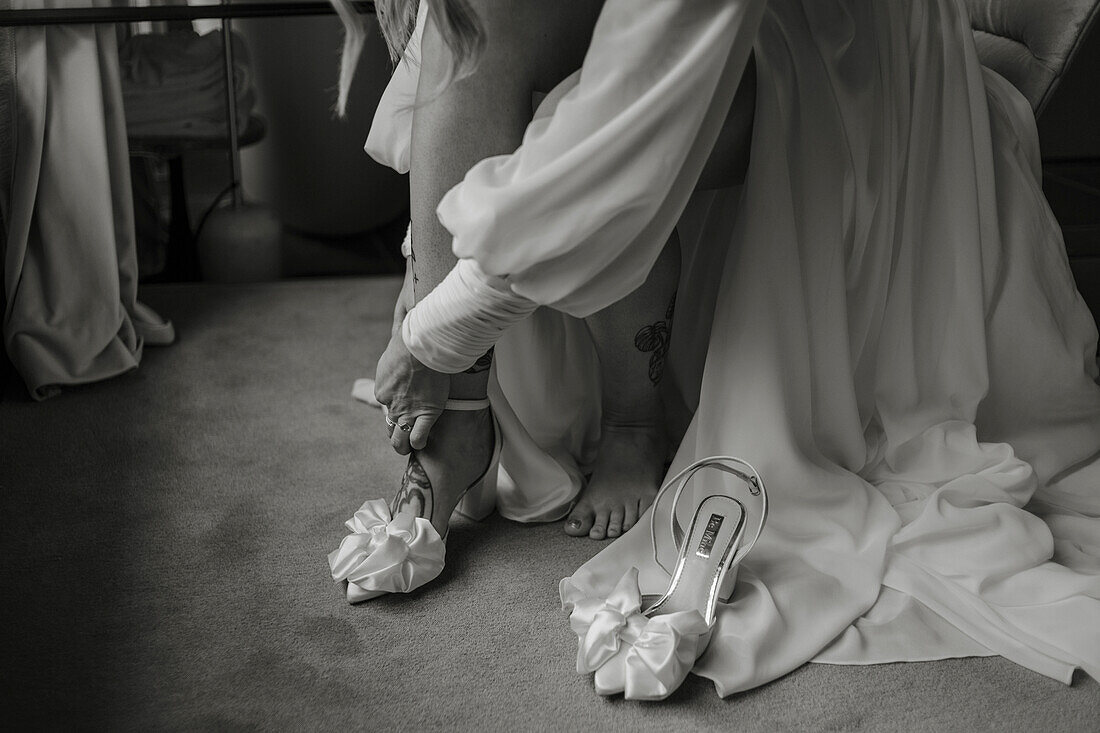 Bride puts on sandals with bows under flowing wedding dress