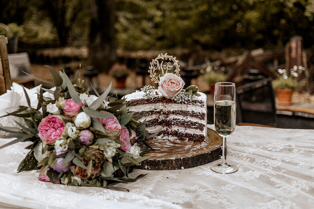 Angeschnittene Hochzeitstorte mit Dekoration, Brautstrauß und Sektglas