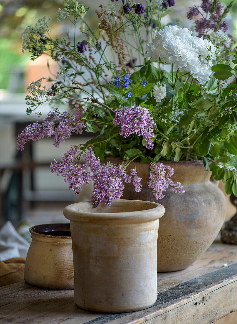 Rustic clay jugs with summer flower bouquet on wooden table