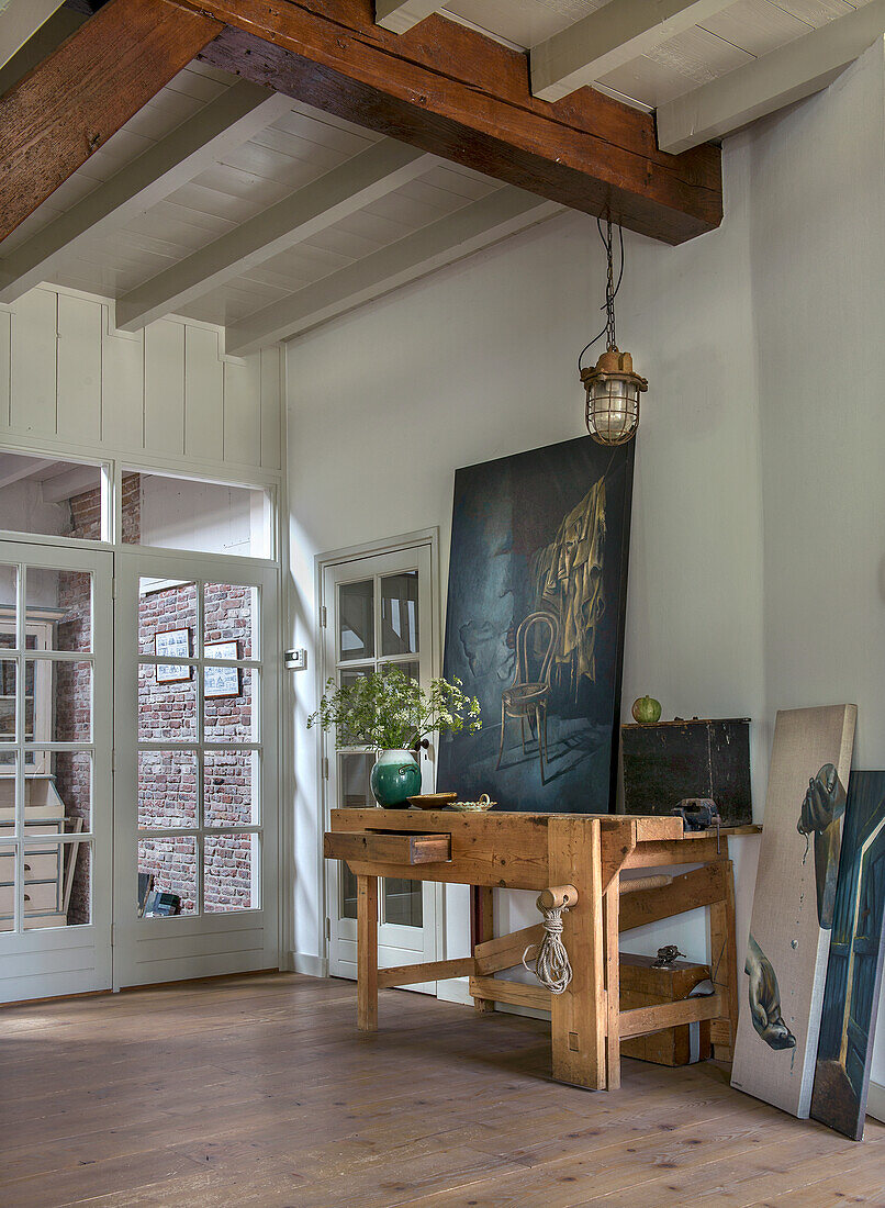 Workbench and painting in light-flooded room with wooden beamed ceiling