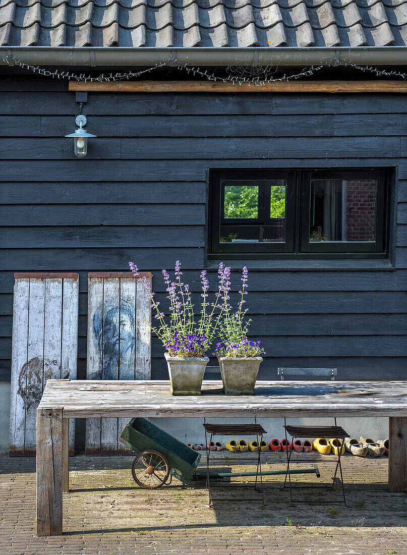 Large wooden table with lavender in pots in front of a dark wooden façade