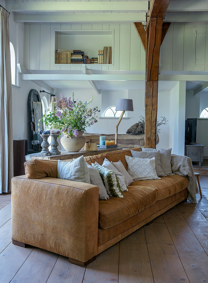 Brown sofa in living room with wooden beams and flower arrangement