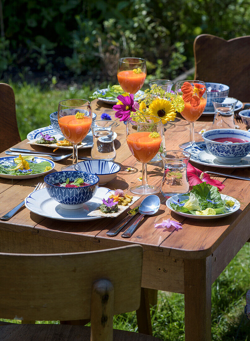 Sommerlich gedeckter Gartentisch mit bunten Blumen und Getränken