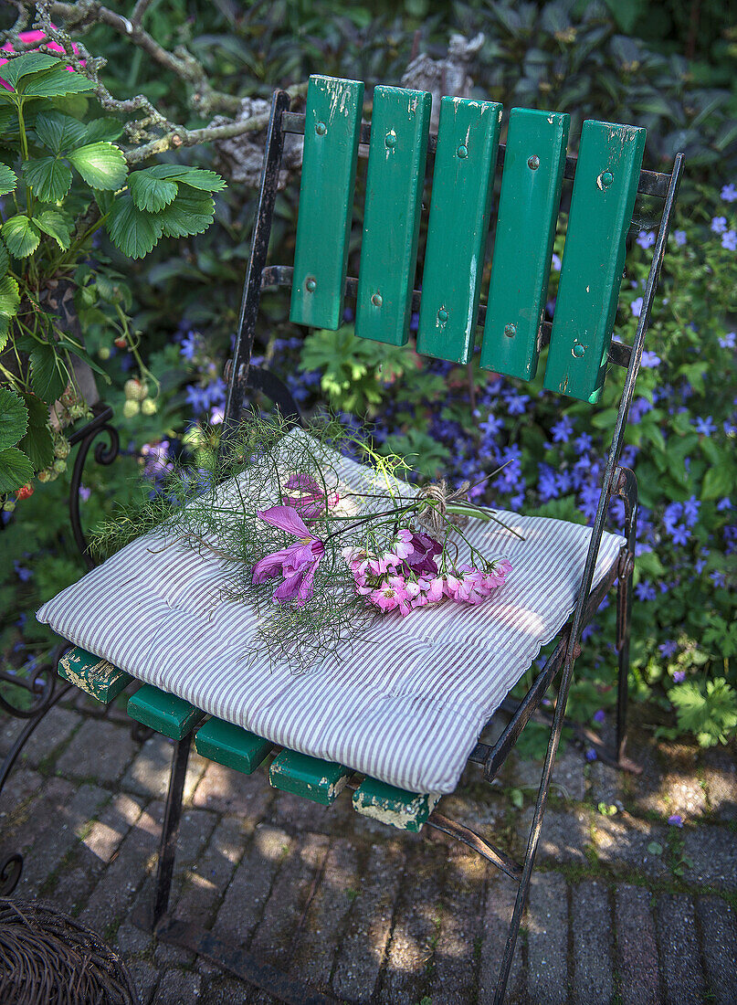 Freshly picked flowers on a green garden chair with striped seat cushion