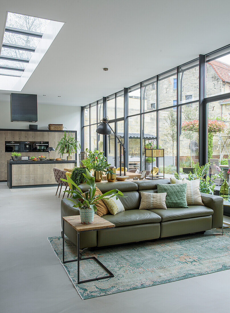 Open-plan living room with kitchen, leather sofa and large windows