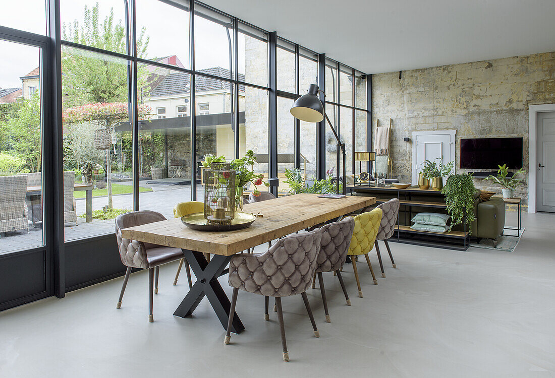 Dining room with long wooden table and upholstered chairs, large window front facing the garden