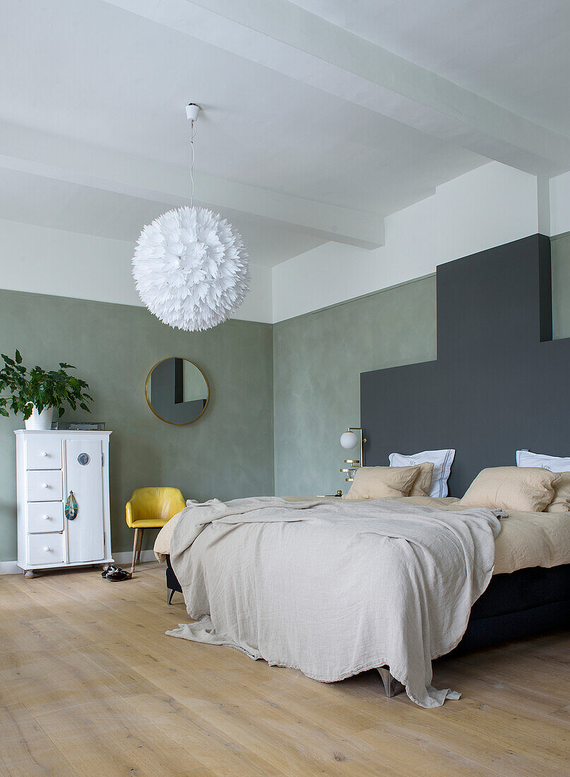 Bedroom with green accent wall, black bed, linen bed linen and modern hanging lamp