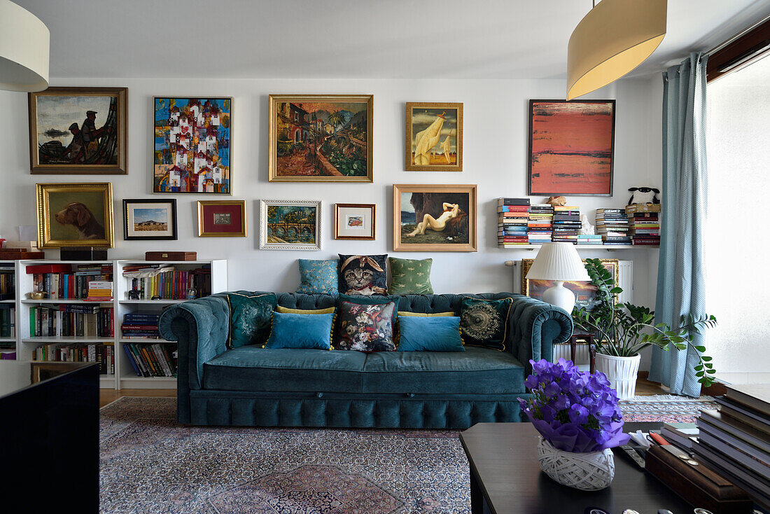 Living room with blue velvet sofa and wall full of paintings
