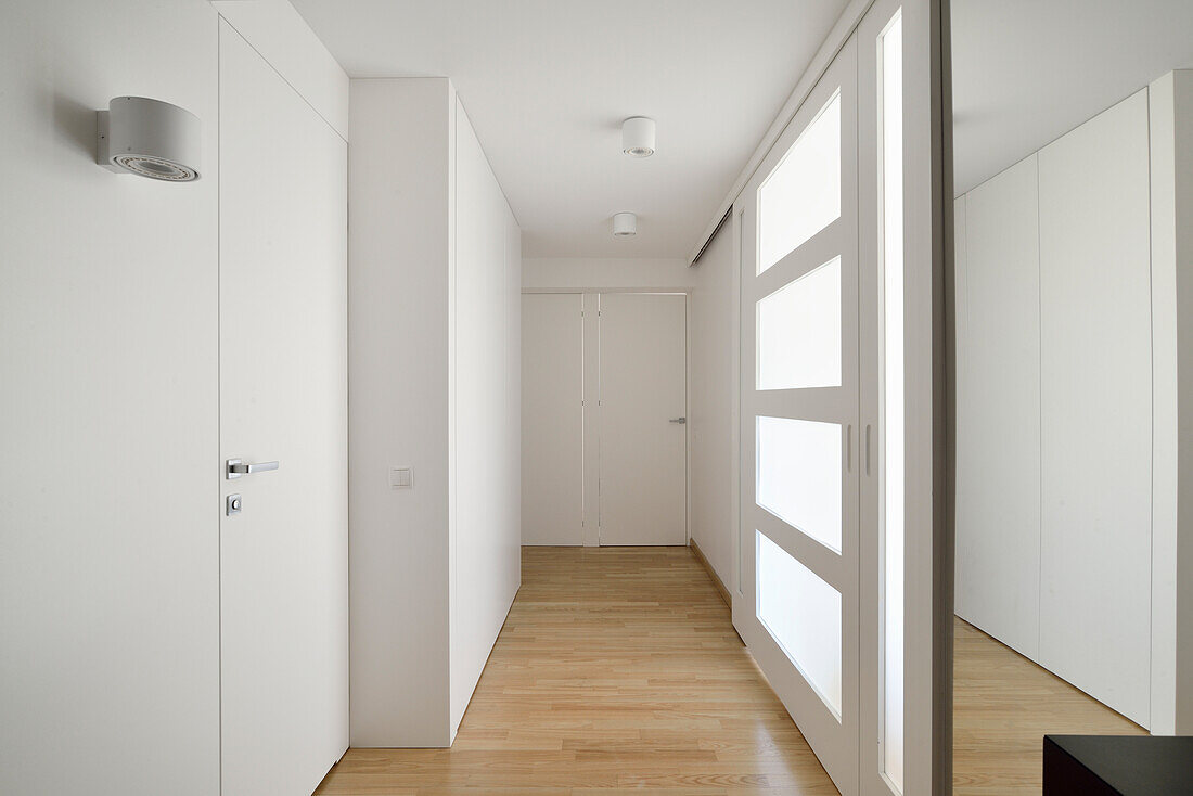 Minimalist hallway with light-colored wooden floor, white walls and glass door