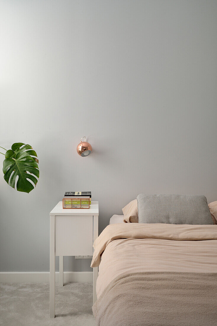 Minimalist bedroom with cream-colored bed linen and copper wall lamp