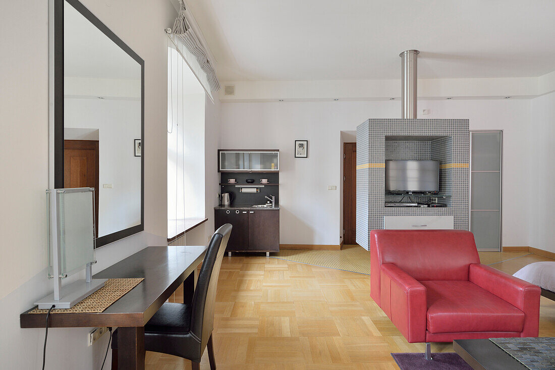 Modern studio interior with workstation, kitchenette and red leather armchair