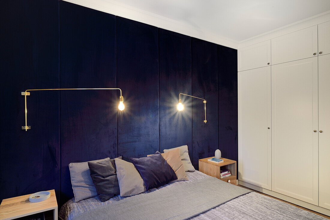 Schlafzimmer mit dunkelblauer Wandverkleidung, Einbauschränken und modernen Wandlampen