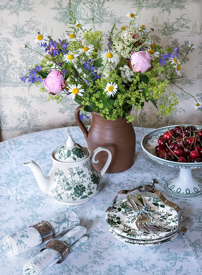 Tisch mit Tellern, Kaffeekanne, Servietten, Blumenvase und Schale mit Kirschen, Landhausstil