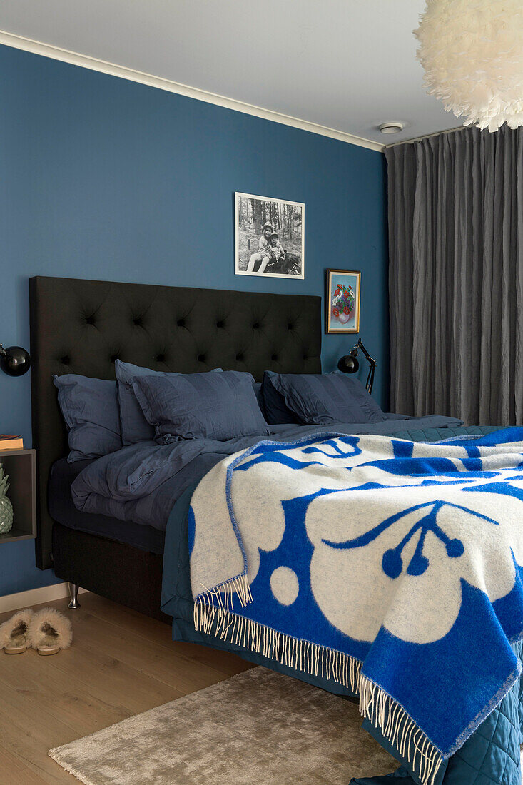 Schlafzimmer mit blauer Wand, Polsterbett und gemusterter Wolldecke in Blau-Weiß