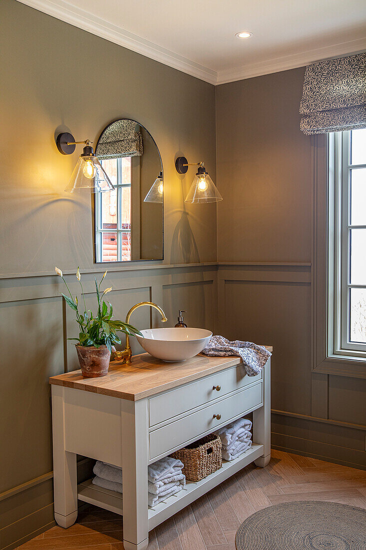 Washbasin with wooden worktop and countertop washbasin in bathroom with wall lights and plant decor