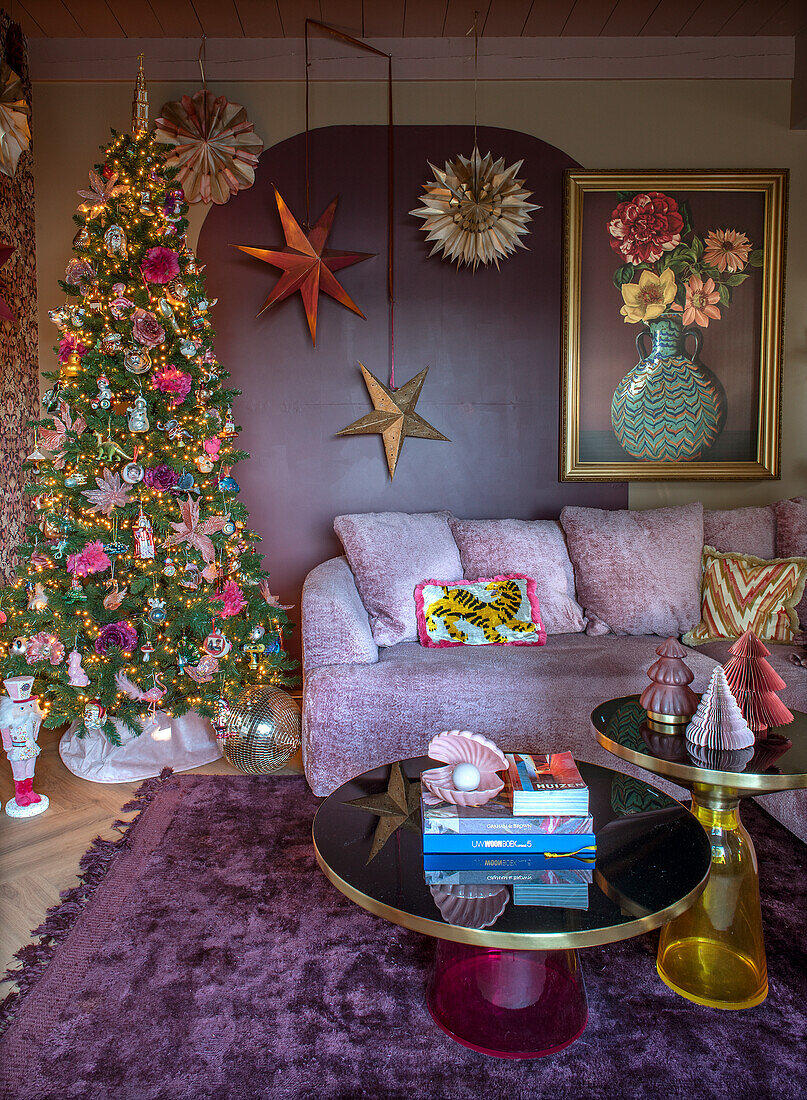 Weihnachtlich dekoriertes Wohnzimmer mit Sofa in Helllila und buntem Baum