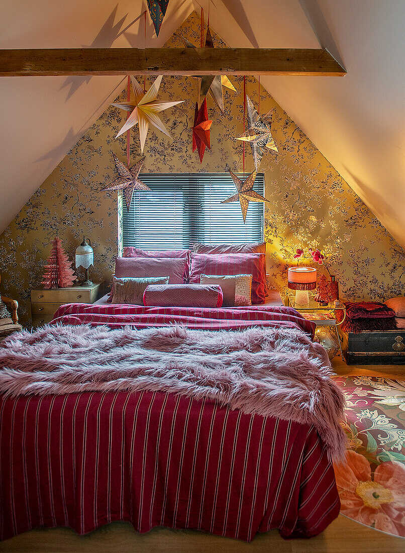 Bedroom under the roof with bed, wooden beams and paper poinsettias