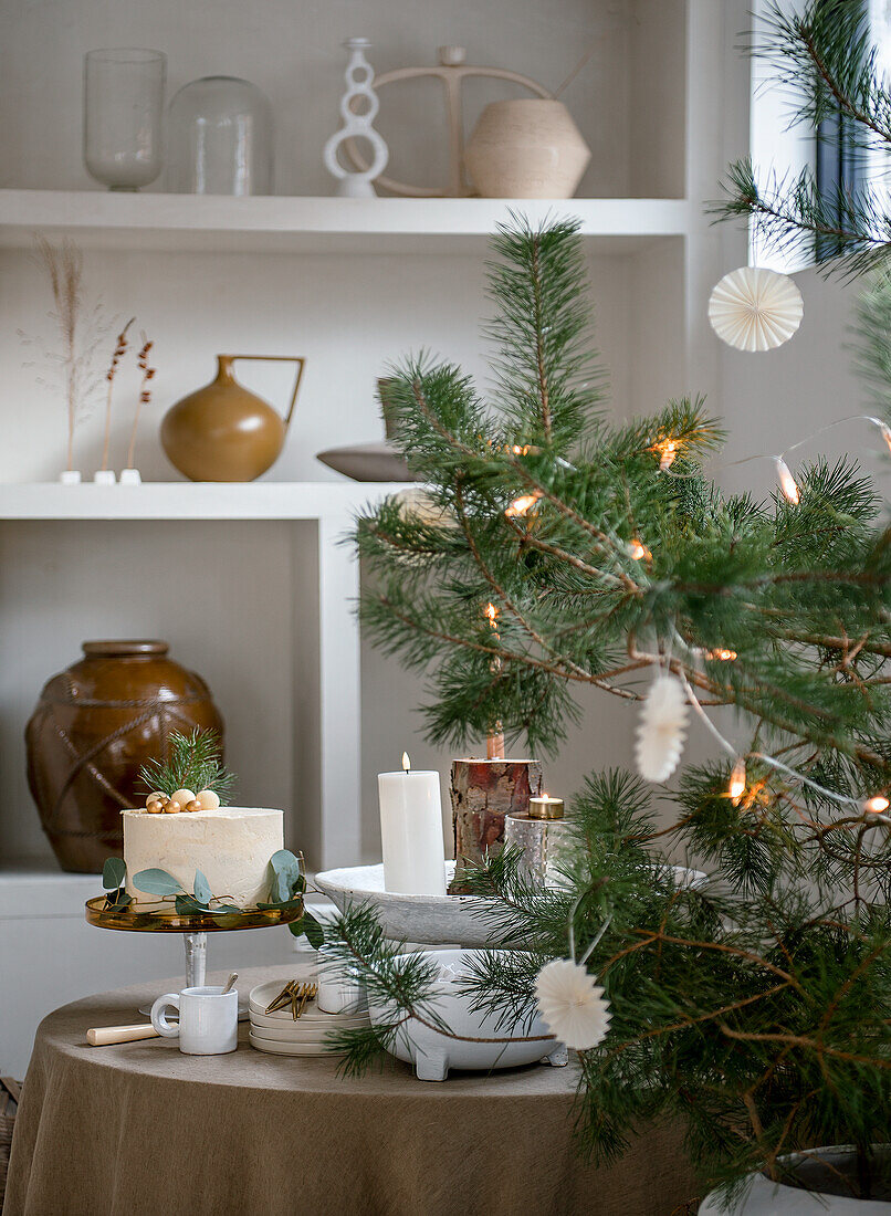 Weihnachtlich dekorierter Tisch mit Torte und Kerzen, daneben geschmückter Baum