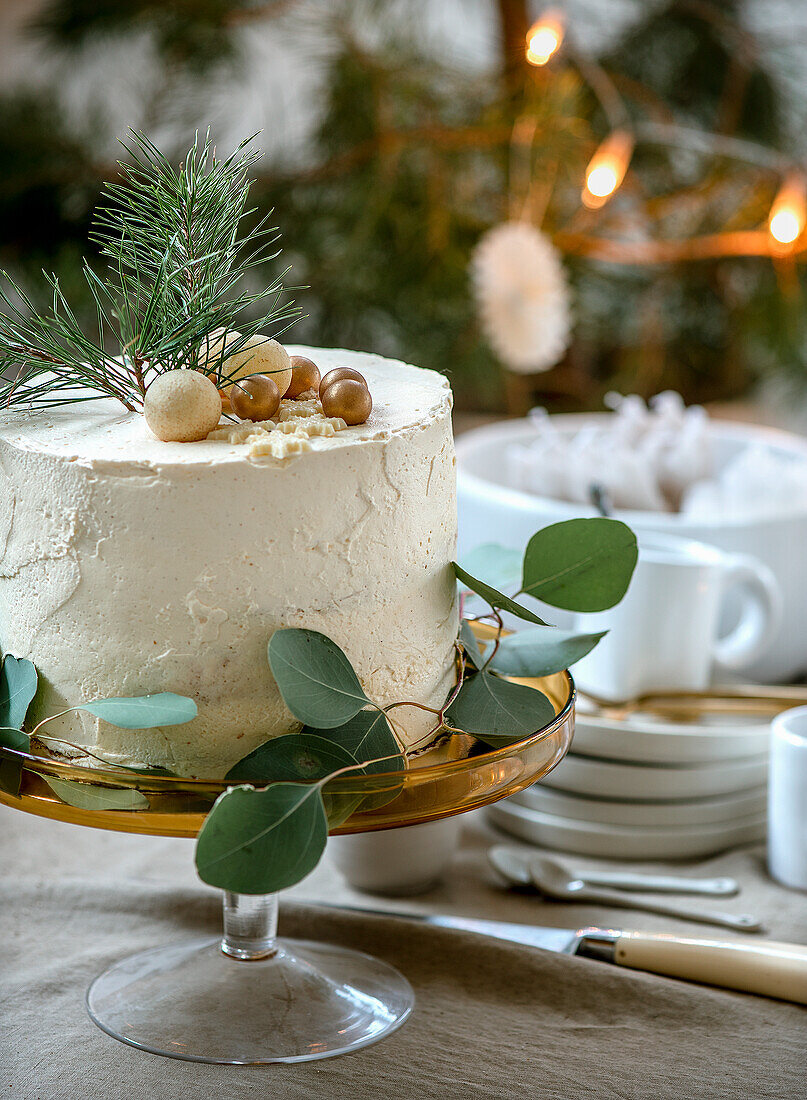 Weihnachtliche Torte mit Zweigen und goldenen Kugeln auf Glastortenständer