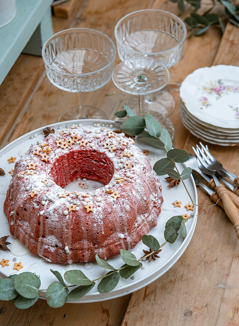 Red and white Gugelhupf on a rustic wooden table, glasses, cake forks and cake plates