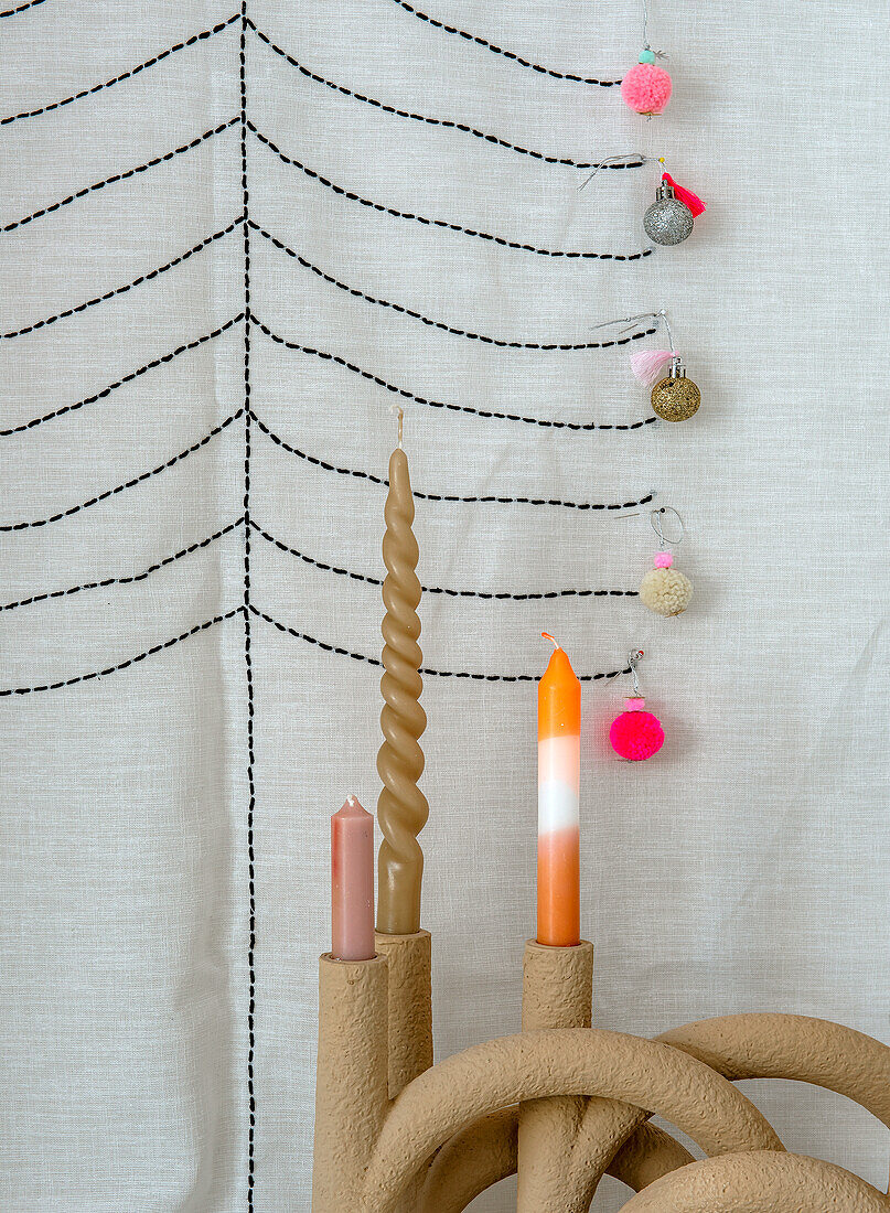 Three candles in a curved candle holder in front of an embroidered fabric background