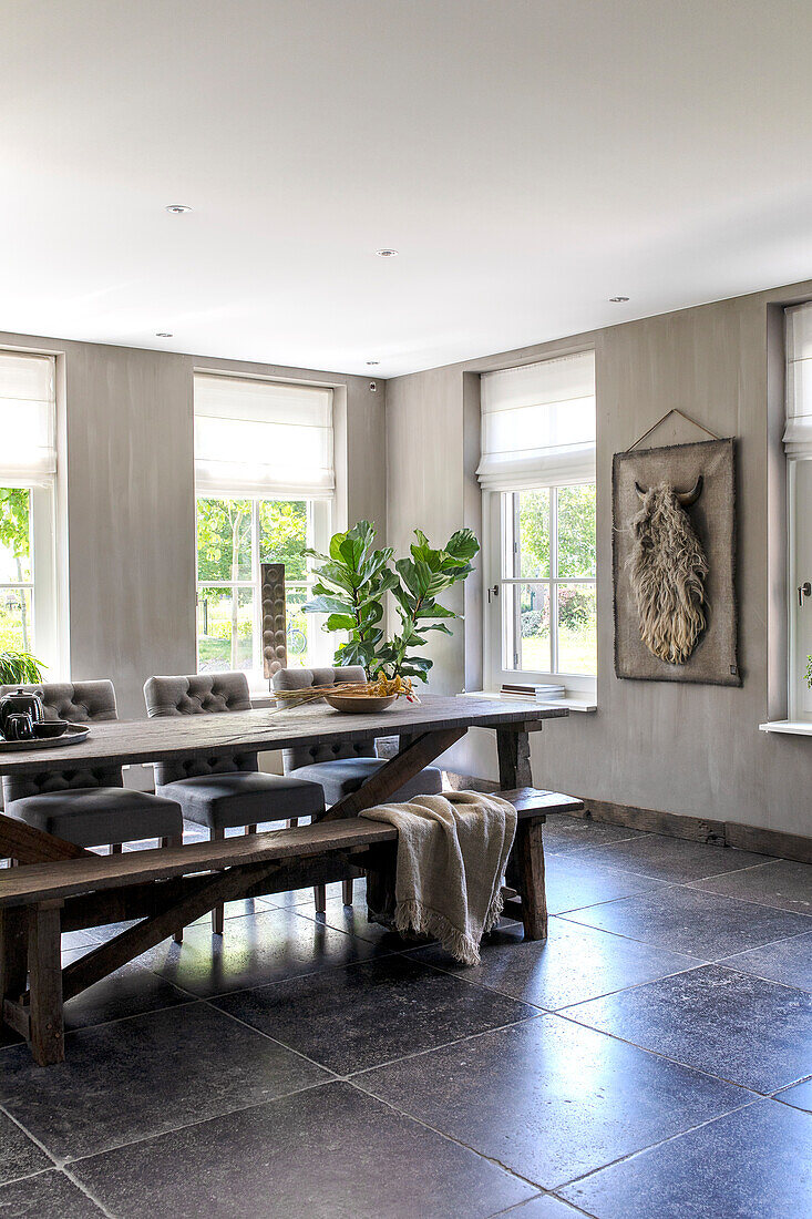 Dining room with rustic wooden table, grey tiles and view of the greenery