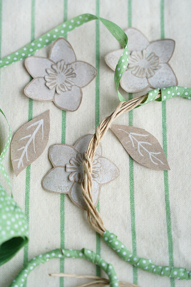 DIY flowers and leaves made from paper and decorative rings wrapped in green ribbon with white dots