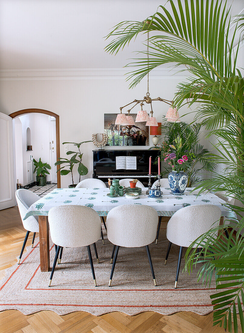 Dining room with dining table, white chairs and piano, surrounded by houseplants