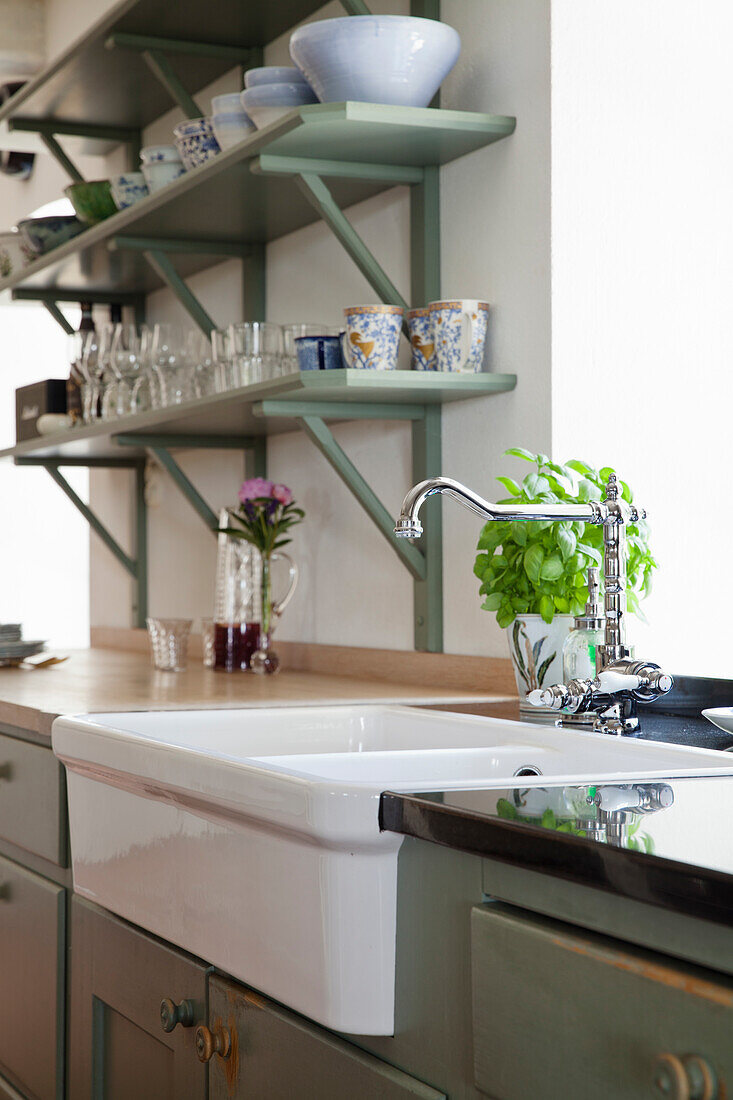 Kitchen with open green shelving and herb pot next to white sink