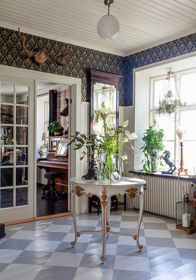 Antique, round table with flower arrangement in a classic hallway with checkered floor