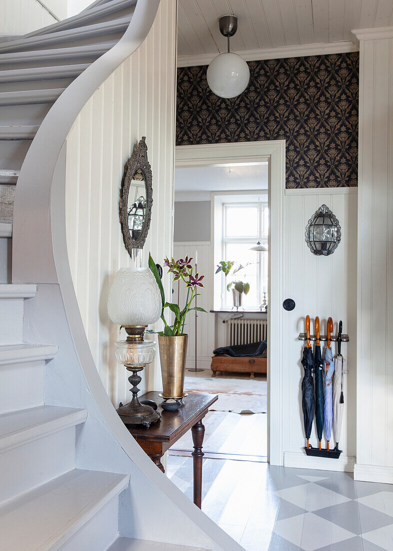 Tiled entrance hall with curved staircase, side table and umbrella stand