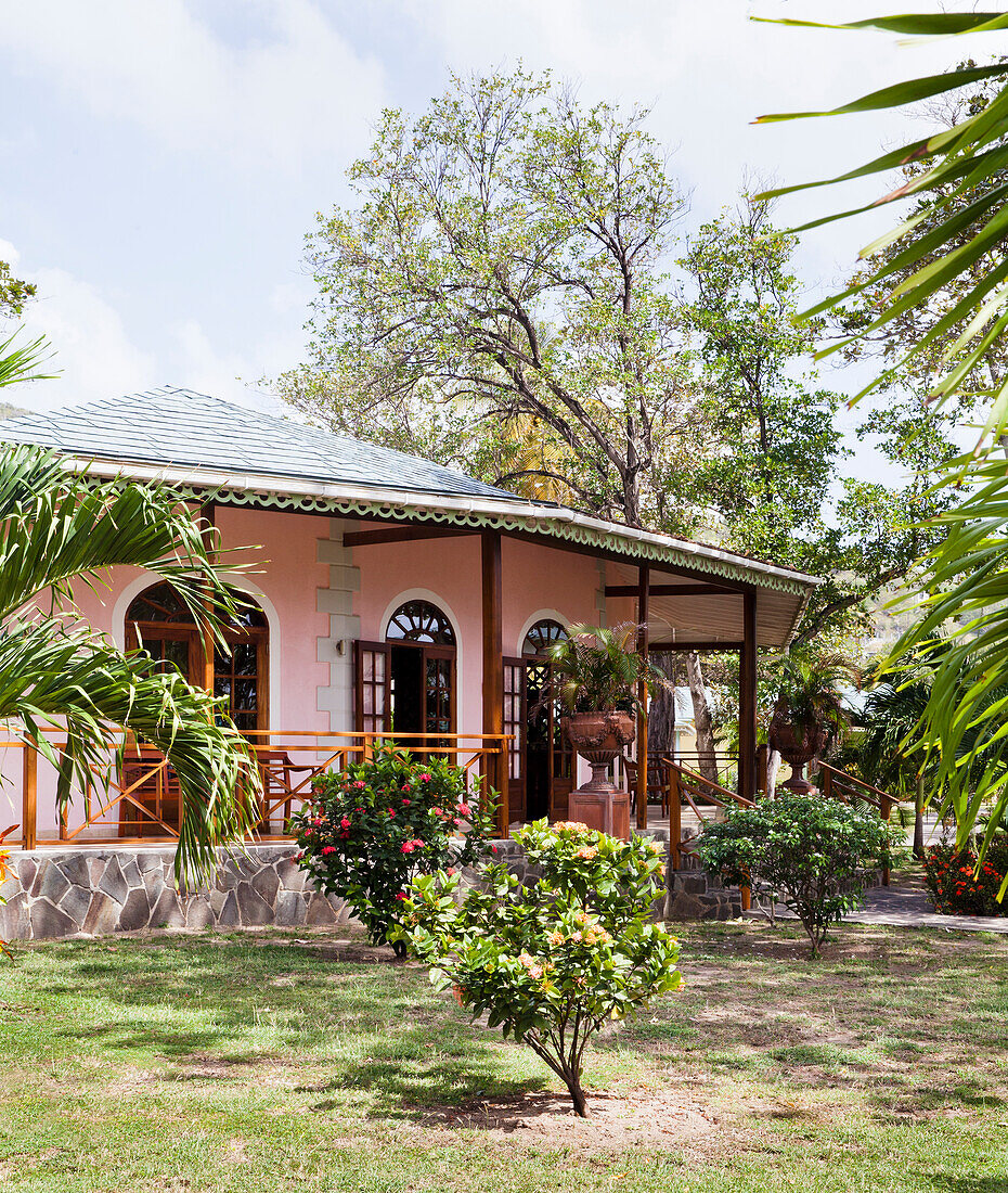 Pink house with wooden veranda and tropical plants in the garden