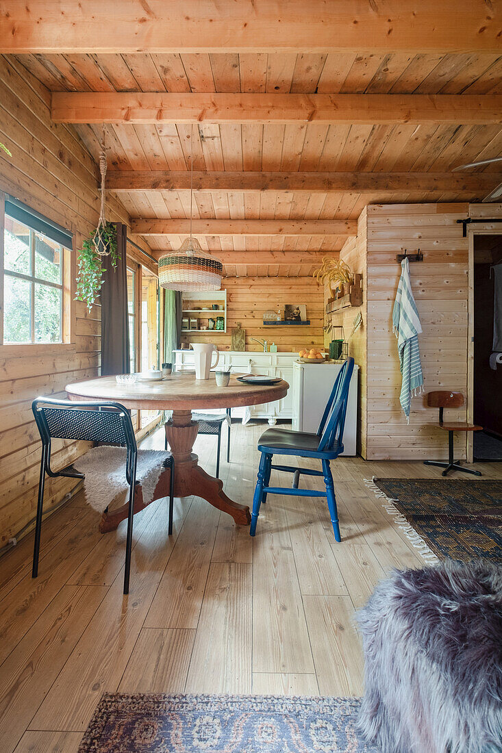 Dining area in rustic wooden hut with round table and various chairs