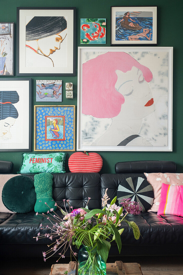 Black leather sofa with cushions in front of dark green wall with colourful artwork