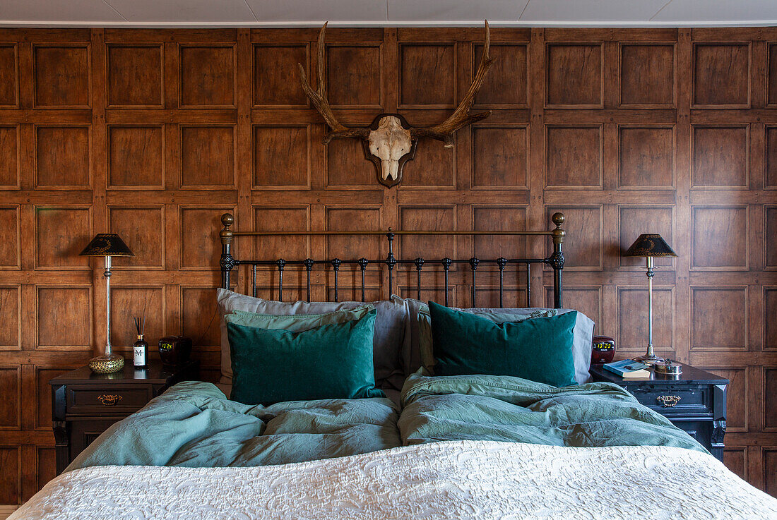 Bedroom with metal bed, wood paneling and antler decoration