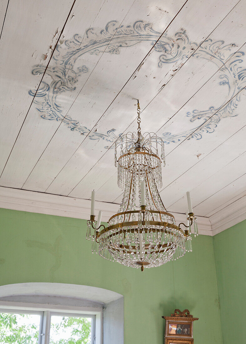 Crystal chandelier with ornate decorations on the wooden ceiling in green-painted room