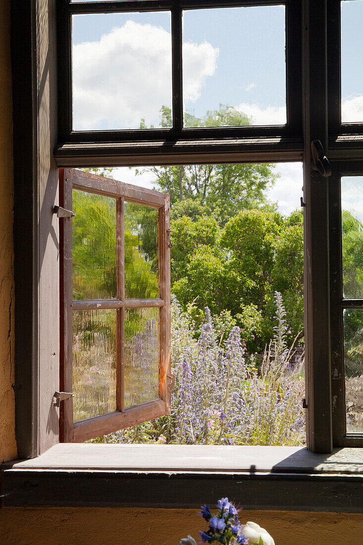 Geöffnete Holzfenster mit Blick in blühenden Sommergarten