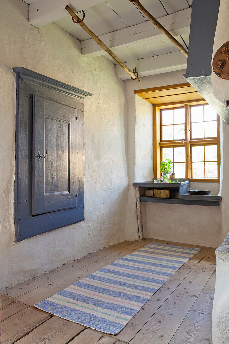 Rustic hallway with wooden floor, blue wall cupboard and striped carpet runner