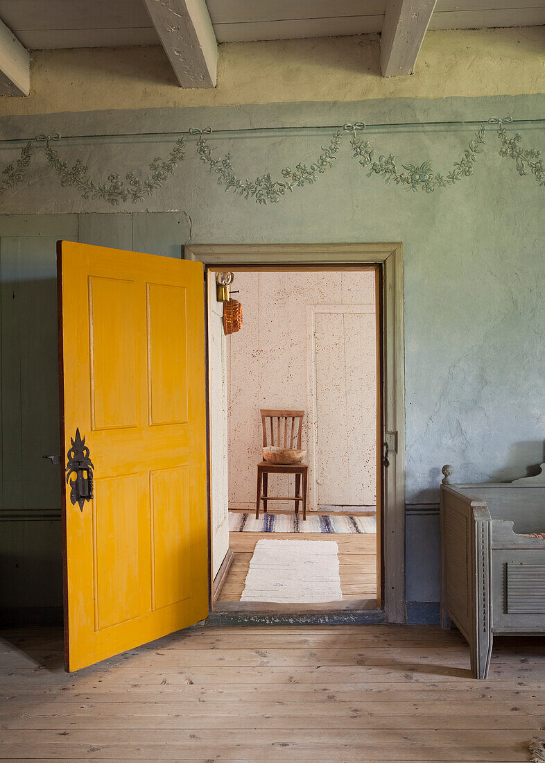 Yellow wooden door opens to a room with wooden floor and chair