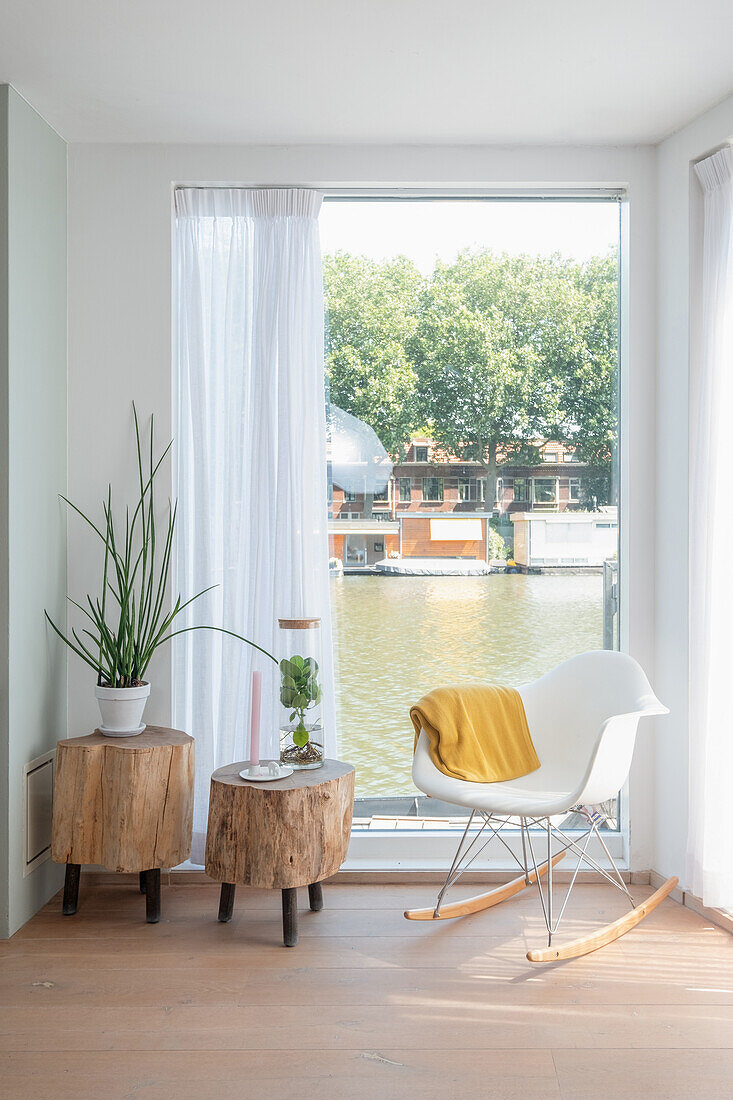 Sitzbereich mit Schaukelstuhl und Baumstamm-Tischchen am Fenster, Blick auf Fluss