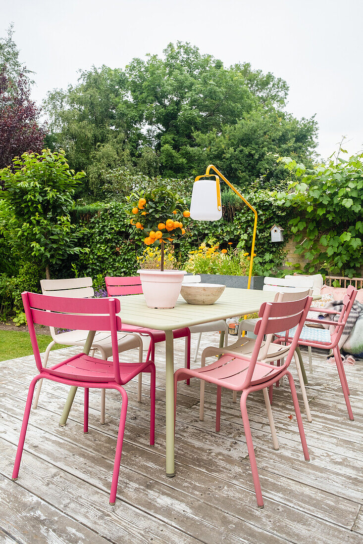 Bunte Metallstühle und Tisch auf Holzterrasse im Garten