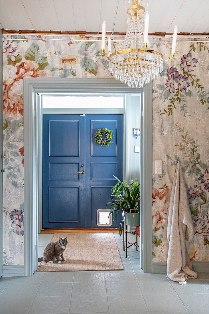 View of hallway with blue entrance door, floral pattern wallpaper and crystal chandelier