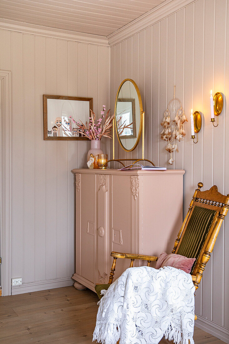 Corner of a room with antique mirror, pink chest of drawers and wooden rocking chair